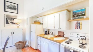 A compact kitchen with white cabinets, a stove, a sink, and a coffee maker. - Charming condo with mountain view, skiing, fireplace, & balcony (Crested Butte)