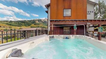A hot tub with a wooden building in the background and a mountainous landscape.
