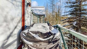 A covered grill outside a building with a metal railing and snow-covered trees in the background. - Main Street condo with mountain view, fireplace, pool & hot tubs - walk to lifts (Breckenridge)