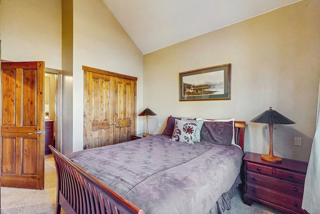 A bedroom with a bed, wooden wardrobe, bedside tables, and a framed picture on the wall.