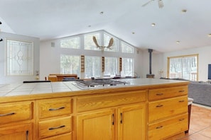 A spacious kitchen with a large island, wooden cabinets, and a central chimney. - Dog-friendly home with large deck, hot tub, woodstove, W/D, & serene setting (Fairplay)
