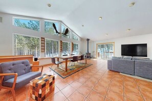 A spacious living area with a fireplace, large windows, a sofa, and a television. - Dog-friendly home with large deck, hot tub, woodstove, W/D, & serene setting (Fairplay)