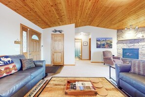 A living room with a wooden ceiling, a stone fireplace, and a view of a mountainous landscape.