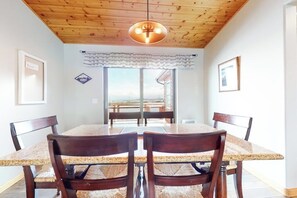 A dining area with a wooden ceiling, a table with chairs, and a view through a glass door.