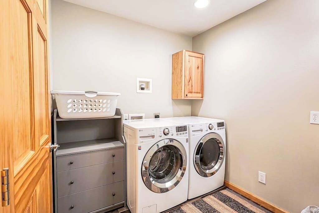 A laundry area with two washing machines, a wooden cabinet, a gray storage unit, and a laundry basket.