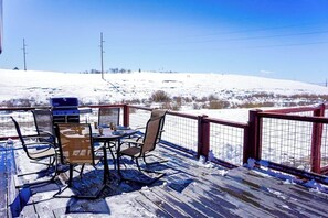 A wooden deck with outdoor furniture, a grill, and a view of a snowy landscape.