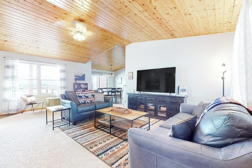 A living room with a wooden ceiling, a television, a sofa, a coffee table, and a patterned rug.