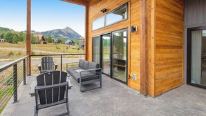 Eine Holzausfachung mit Balkon, zwei Stühlen, einer Couch und einem großen Schiebeglastür.