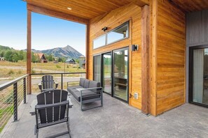 A wooden exterior with a balcony, two chairs, a sofa, and a large sliding glass door. - Modern mountain retreat with decks, kitchens, & kid-friendly items - near skiing (Crested Butte)