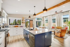 A modern kitchen with a central island, white cabinetry, and pendant lighting. - Modern mountain retreat with decks, kitchens, & kid-friendly items - near skiing (Crested Butte)