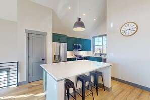 A modern kitchen with teal cabinets, a large island with stools, a stainless steel refrigerator, and a microwave. - Relax, Recharge, and Explore – Your Perfect Mountain Retreat in Granby, CO (Granby)