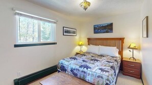 Un dormitorio con una cama grande, dos lámparas de noche, un cuadro en la pared y una ventana con persianas.