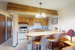 A kitchen with wooden cabinets, a white stove, a microwave, and a wooden island with bar stools. - Quaint getaway steps from Main Street with fireplace & full kitchen (Winter Park)