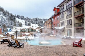 A hot spring area with lounge chairs, a pool, and buildings with balconies.