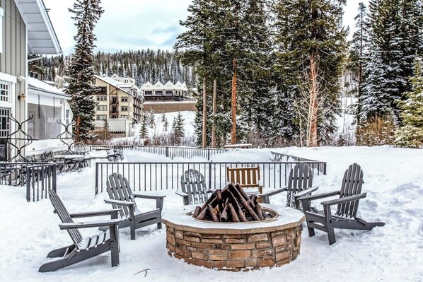 A snow-covered outdoor seating area with Adirondack chairs and a stone fire pit.