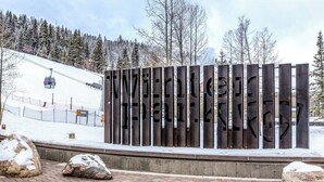 Puinen kyltti, jossa lukee teksti ”TENNISBERG”, sijaitsee vuoristoisella alueella, ja taustalla näkyy hiihtohissi.