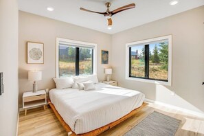 Ein Schlafzimmer mit einem großen Bett, zwei Nachttischen, einem Deckenventilator und zwei Fenstern mit Blick ins Freie.