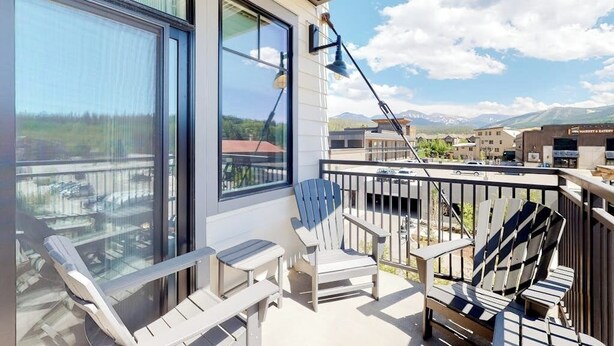 En balkon med udsigt til bjerge, en stol, et bord og en lampe.