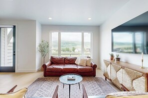 Ein Wohnzimmer mit einer Ledersofa, einem runden Couchtisch und Blick auf eine grüne Landschaft durch große Fenster.