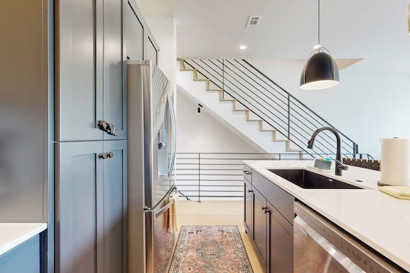 Eine moderne Küche mit eingebautem Geschirrspüler, einem Edelstahl-Kühlschrank und einer Treppe, die auf einen Balkon führt.