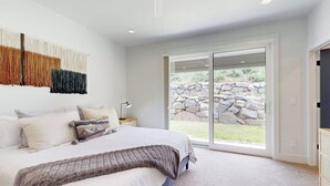 Un dormitorio con una cama grande, un muro de piedra en el exterior y una puerta corrediza de vidrio.