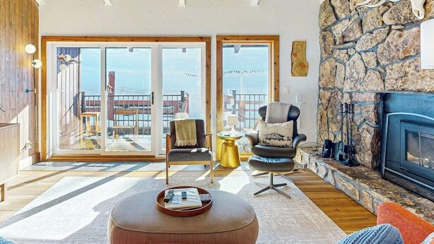 Ein Wohnzimmer mit Kamin aus Stein, großem Fenster mit Aussicht, gemütlicher Sitzecke und Holzboden.