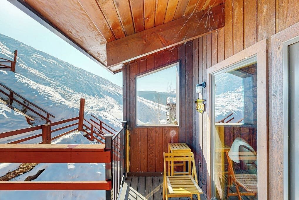 Un pontile in legno con vista su montagne innevate, una panchina di legno e una porta vetrata.