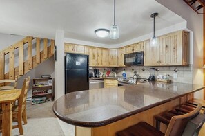 A kitchen with wooden cabinets, a central island, a refrigerator, and a microwave. - Cozy condo with easy ski access, W/D, fully stocked kitchen & great location (Breckenridge)