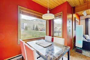 Ein Essbereich mit Tisch und Stühlen, große Fenster mit Blick auf eine Berglandschaft und eine moderne Leuchte.