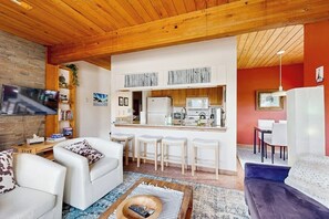 Ein modernes Wohnzimmer mit Küchenzeile, Holzboden und einem an der Wand befestigten Fernseher.