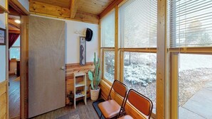 Interior de madeira com uma porta, um cacto e duas cadeiras perto de uma janela.