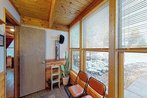 Un interior de madera con una puerta, un cactus y dos sillas junto a una ventana.