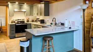 Cozinha com armários cinza, uma ilha central com banquetas, uma lixeira e uma pia.