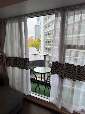 Ein Zimmer mit Balkon, einem runden Glastisch und Blick auf ein mehrgeschossiges Gebäude.