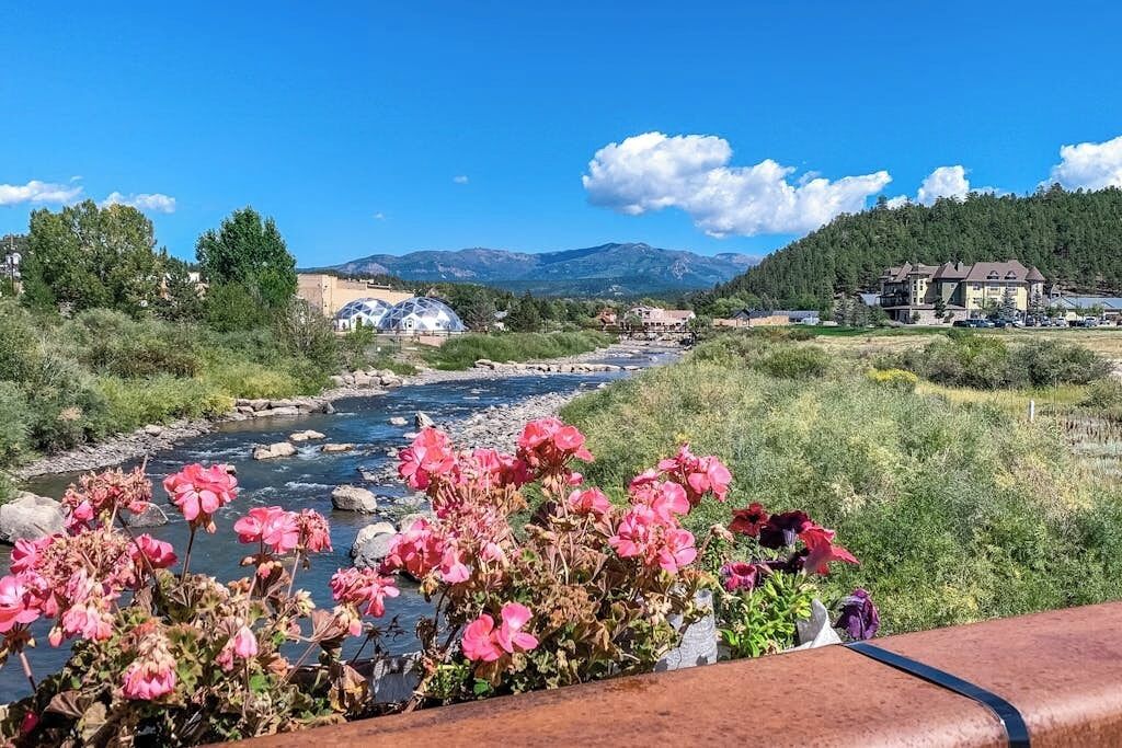A river flowing through a landscape with buildings and mountains in the background.