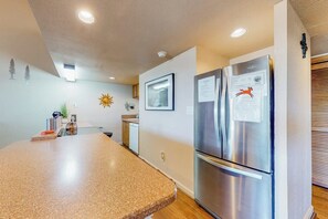 A kitchen with a granite countertop, stainless steel refrigerator, and recessed ceiling lights.
