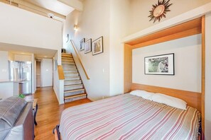 A bedroom with a bed, a wooden headboard, a staircase, and a hallway leading to a kitchen.