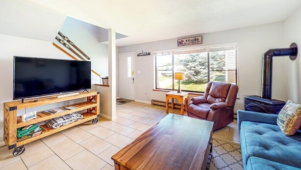 Een woonkamer met een televisie op een houten standaard, een leren fauteuil, een blauwe bank en een open haard.