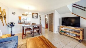 Een woonkamer met een televisie, houten meubels, een eethoek en een trap.