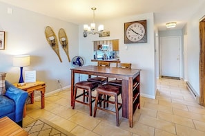 A dining area with a wooden table and four stools, a clock on the wall, and a fan on the floor. - Two-story, dog-friendly townhouse with a washer/dryer & a full kitchen (Pagosa Springs)