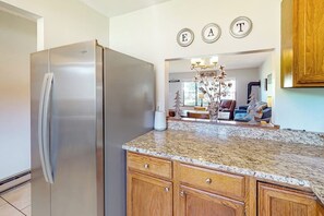 A kitchen with a stainless steel refrigerator, granite countertop, wooden cabinets, and a chandelier. - Two-story, dog-friendly townhouse with a washer/dryer & a full kitchen (Pagosa Springs)