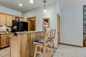 Eine Küche mit Holzschränken, einem schwarzen Kühlschrank, einer Holzinsel mit Barhocker und einer Wand mit Steinverkleidung.