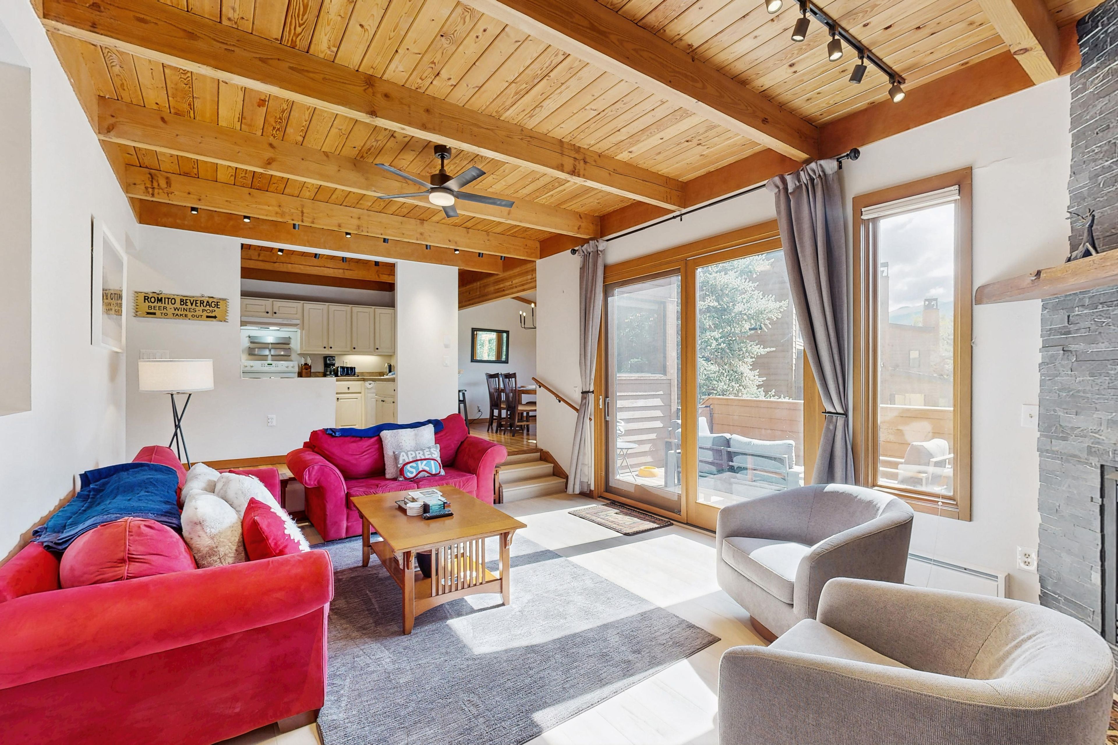 A spacious living area with a wooden ceiling, a red sofa, a grey armchair, and a dining area in the background.