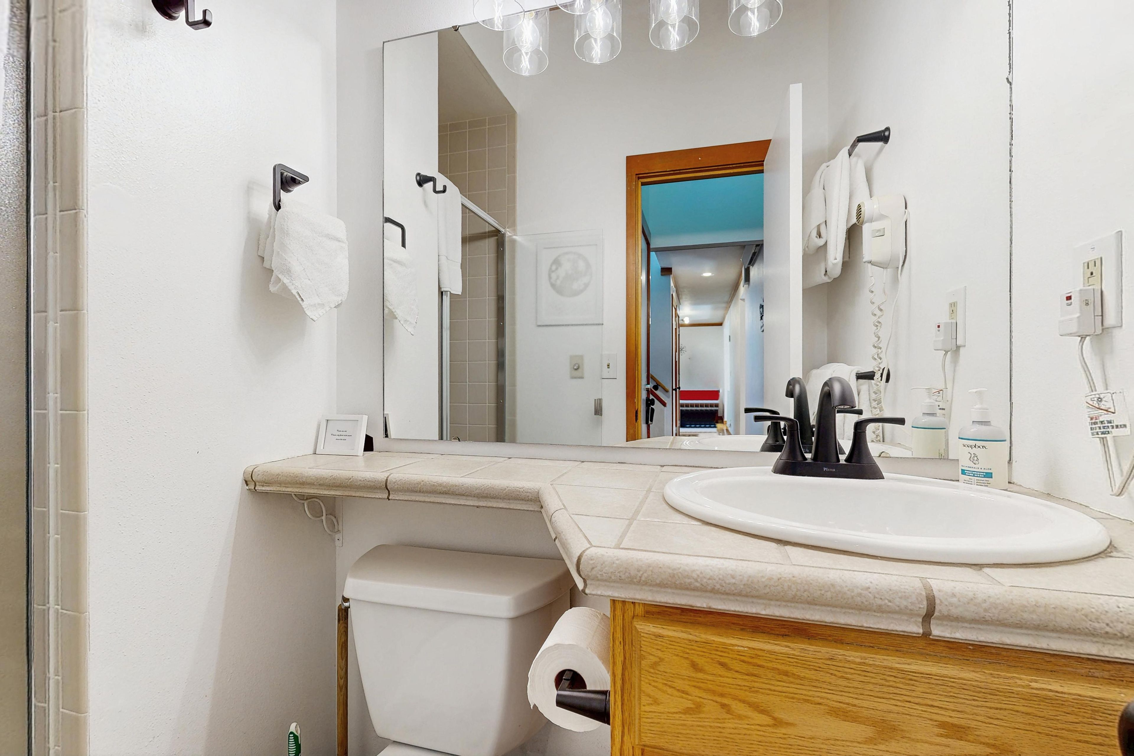Une salle de bain avec un lavabo blanc, un miroir, un porte-serviettes, des toilettes et un espace douche.