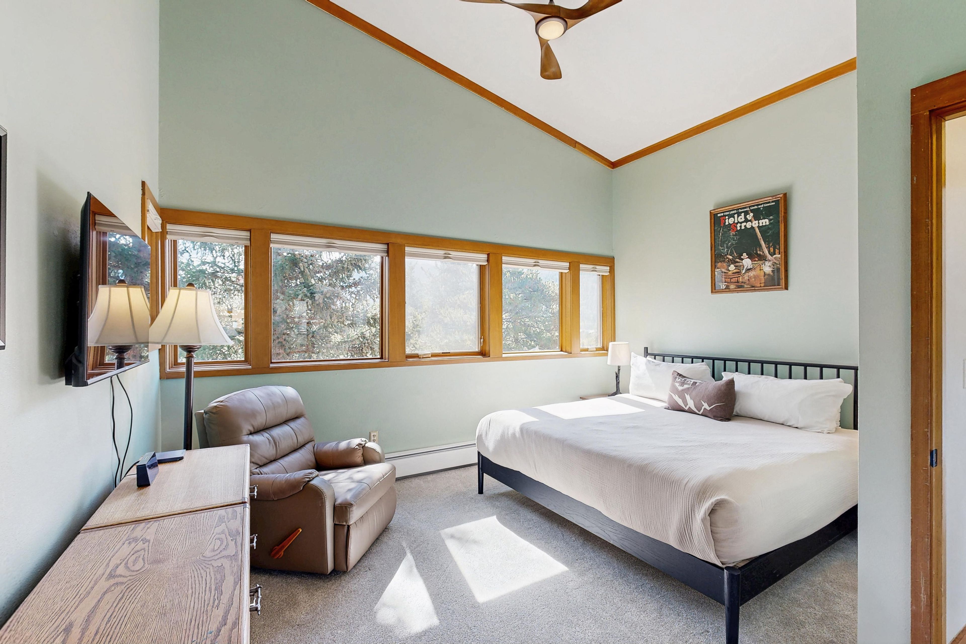A bedroom with a bed, a chair, a desk, a lamp, a ceiling fan, and a poster on the wall.