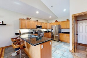 A kitchen with wooden cabinets, stainless steel appliances, and a granite countertop island with bar stools. - Convenient condo with fireplace & WiFi - walk to rec center pool, tennis & town (Pagosa Springs)