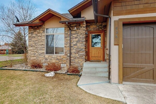 A two-story house with a stone facade, a wooden front door, and a garage door. - Convenient condo with fireplace & WiFi - walk to rec center pool, tennis & town (Pagosa Springs)