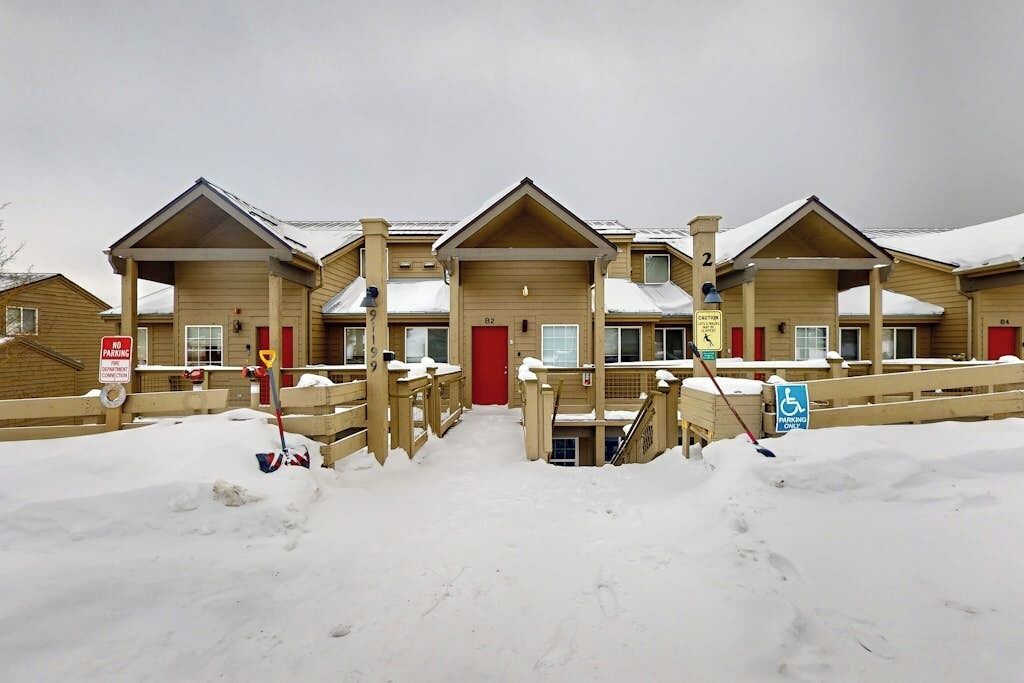 A row of wooden cabins with a red door, a wheelchair-accessible ramp, and a no parking sign.