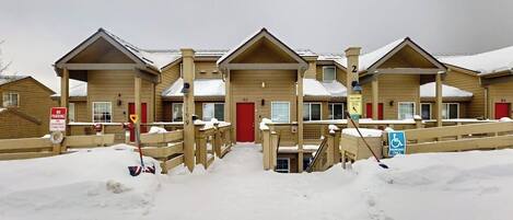 A row of wooden cabins with a red door, a wheelchair-accessible ramp, and a no parking sign.