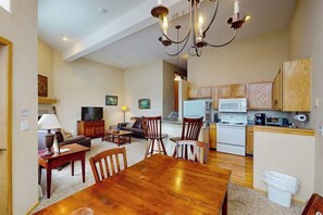 A spacious living area with a wooden dining table, a sofa, and a TV. There is a kitchen with wooden cabinets and a microwave. - Dog-Friendly Home with Trail Access, Gorgeous Views (Silverthorne)